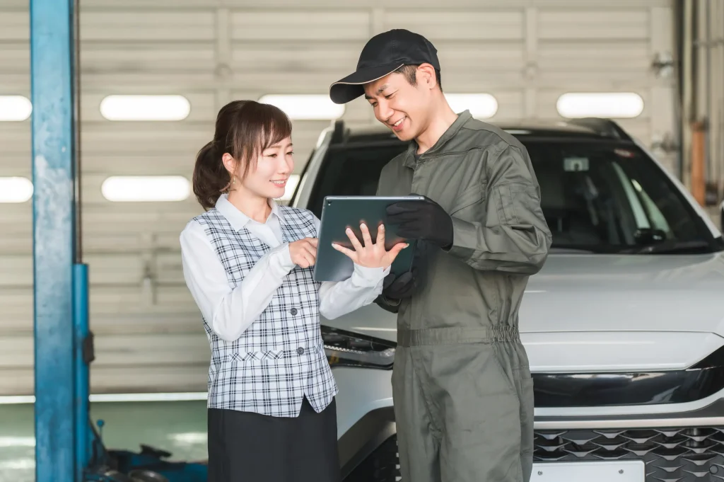 整備工場のピットでタブレットを確認する整備士と受付担当